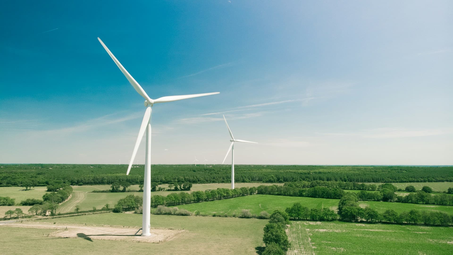 Wind turbines across fields beneath a blue sky